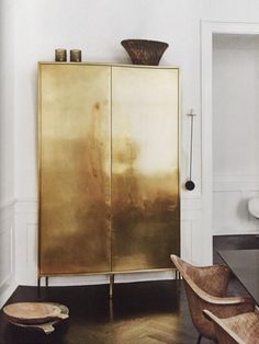 a gold cabinet in the corner of a room with two chairs and a vase on top