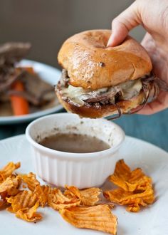 a person is dipping some kind of sauce into a hamburger on a plate with chips