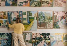 a woman standing in front of a wall with paintings on it and holding onto a pair of scissors