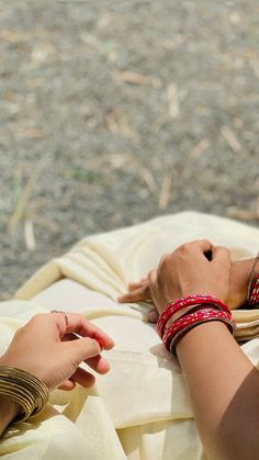 two women are touching each other's hands while sitting on the ground with bracelets around their necks