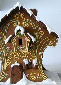 a gingerbread house decorated with icing and snow on the roof, in front of a white wall