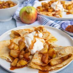 apple pie crepes with whipped cream and apples in the background on a blue tablecloth