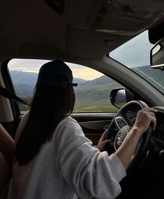 a woman driving a car with mountains in the background