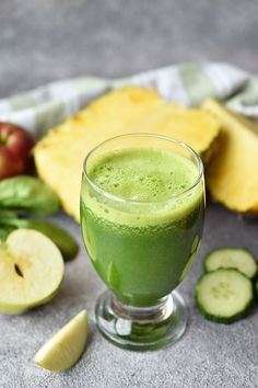 a glass filled with green liquid next to sliced fruit