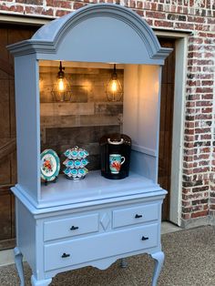 a blue cabinet with two plates and a coffee maker on it in front of a brick wall