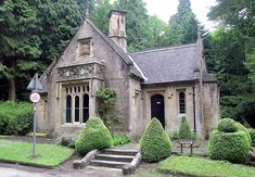 an old stone building with trees and bushes around it's front entrance, surrounded by greenery