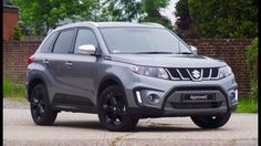 the front end of a silver suzuki suv parked in a driveway next to a brick wall