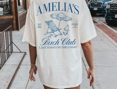 a woman walking down the street wearing a white t - shirt that says ameli's beach club