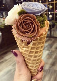 a woman holding an ice cream cone with chocolate frosting and flowers in it's center