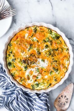 a quiche with cheese and broccoli in a white pie dish on a marble surface