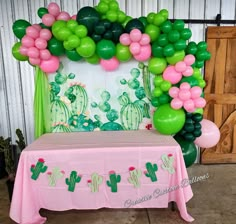 a table topped with a pink and green cake covered in balloons next to a cactus themed backdrop