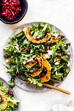 two plates filled with salad next to a bowl of pomegranates on the side