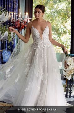 a woman in a wedding dress holding a bouquet and standing next to a chandelier