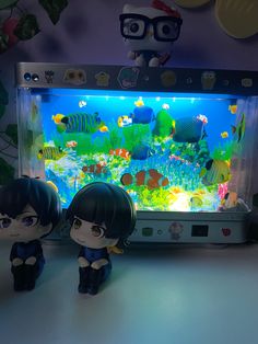 two small figurines sitting next to an aquarium