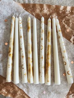 five white candles are lined up on a piece of paper with gold stars and moon designs