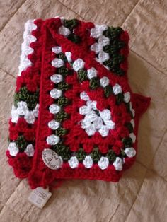 a crocheted red and white blanket laying on top of a bed next to a tag