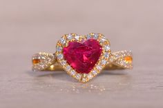 The Lovers Leap: Heart Shaped Natural Ruby and Diamond Ring in Yellow Gold. This stunning ring features a vivid red 2.00-carat heart brilliant-cut natural heated ruby at its center. Surrounding the ruby is a halo of round brilliant-cut natural diamonds, which extend into the crossover shank. The diamonds have a total weight of 0.50 carats, adding a dazzling sparkle to the piece. Crafted in 14-karat yellow gold, the ring is currently a size 6.75 but can be resized to fit any finger for an additio Luxury Heart Cut Ruby Ring, Red Diamond Heart Ring Fine Jewelry, Red Heart Ring With Center Stone, Red Diamond Heart Cut Ring, Heart-shaped Red Ruby Ring With Diamonds, Valentine's Day Ruby Ring With Diamond Halo Setting, Luxury Ruby Ring With Diamond For Valentine's Day, Heart Cut Lab-created Ruby Ring, Luxury Diamond Ruby Ring For Valentine's Day