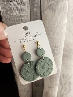 a pair of green and gold earrings with flowers on them, sitting in front of a white card