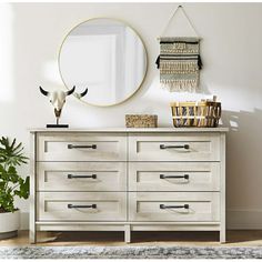 a white dresser topped with lots of drawers next to a mirror and potted plant