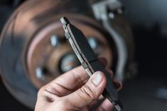 a person holding a piece of metal in front of a wheel with the brake assembly on it