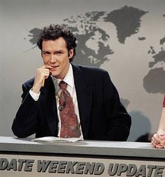 a man and woman sitting at a desk with a world map in the back ground