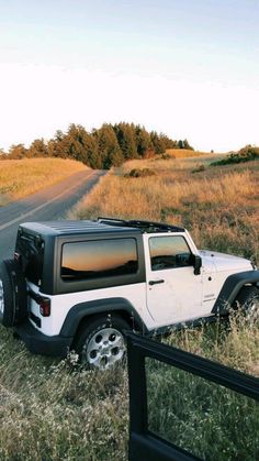 a white jeep parked on the side of a road next to a field with tall grass