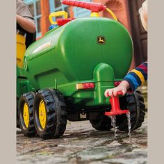 two children playing with a toy tractor and water sprinkler on the ground