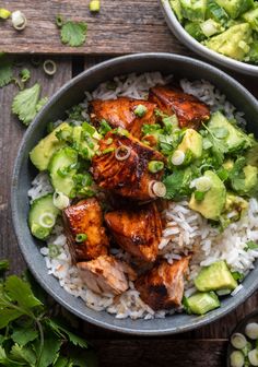 two bowls filled with rice, chicken and avocado on top of a wooden table