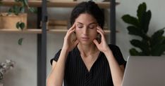 a woman sitting at a desk with her head in her hands while looking at a laptop