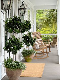 a porch with rocking chairs and potted plants on the front porch, along with hanging lanterns