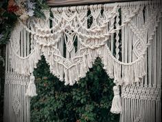 a white macrame hanging from the side of a wooden structure with flowers and greenery around it