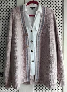 a pink and white cardigan sweater hanging on a wall with an open jacket over it