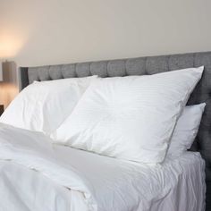 a bed with white sheets and pillows on top of it next to a night stand