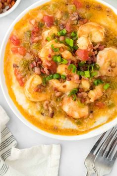 a bowl filled with shrimp and grits on top of a white table next to silverware