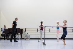 some people are practicing ballet in a large room with white walls and black railings