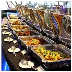 many trays of food are lined up on a buffet table with plates and silverware