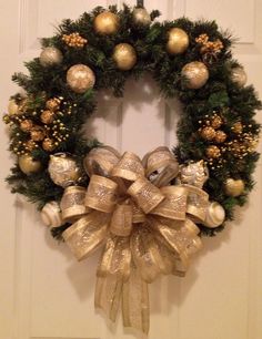 a wreath hanging on the front door decorated with gold and silver balls, pine cones, and bows