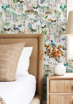 a white vase with flowers on top of a bed next to a night stand and nightstand