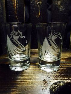 two glasses sitting on top of a wooden table next to each other, one with a horse drawn on it