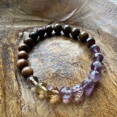 Well Being Bracelet  Natural Wood, Bronzite, Melody Stone, + Ametrine  8 mm Healing Energies: calm, stress relief, intuition, harmony, wellness, creativity, courage, love, grounding Mantra: The healthy habits I choose promote a lifetime of peace, health + wellness. Melody Stone is also interchangeably called Super Seven. Super Seven refers to the 7 highest vibing stones: Amethyst, Quartz Crystal, Smoky Quartz, Cacoxenite, Rutile, Geothite and Lepidocrocite.  Ametrine is a naturally occurring sto Grounding Mantra, Ametrine Jewelry, Purple Crystal Bracelet, Gemstone Chips Bracelet, Amethyst Quartz Crystal, Rainbow Gemstones, Crystal Healing Stones, 3rd Eye, Natural Stone Jewelry