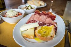 a white plate topped with meats and cheese next to bowls of food on a table