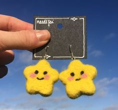 a pair of small yellow stars hanging from the ear of someone's hand, against a blue sky with clouds