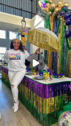 a woman standing in front of a table with balloons and streamers on it at a mardi gras party