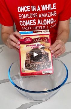 a person holding a box of cake mix in front of a glass bowl on a table