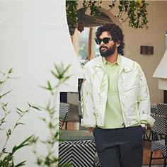 a man wearing sunglasses and a green shirt standing in front of a table with chairs