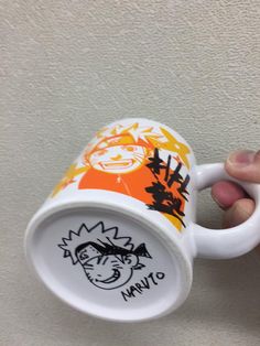 a hand holding a coffee cup with an orange and black cartoon on it's side