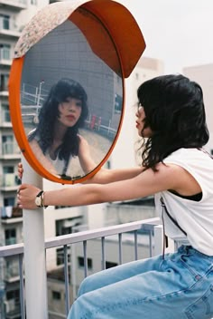 a woman sitting on top of a metal pole next to a round mirror with her reflection in it