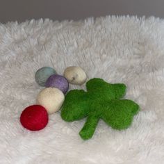 three felt balls and a green leaf laying on a white furnishing area next to each other