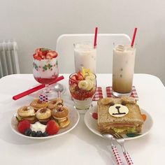 a white table topped with two plates of food and glasses of milkshake next to each other