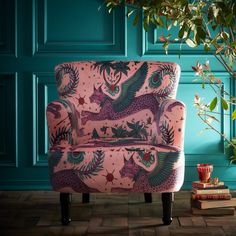 a pink chair sitting in front of a blue wall with green plants and books on the floor